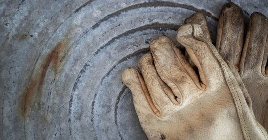 A close-up of a pair of dirty leather work loves. The gloves are sitting on a stainless steel surface.