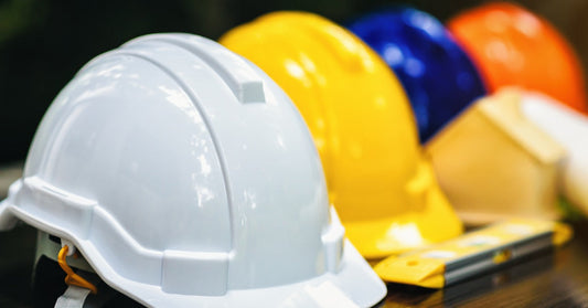 A table with four hard hats sitting in a row. The hats are white, yellow, blue, and orange. There's a pocket knife in front.