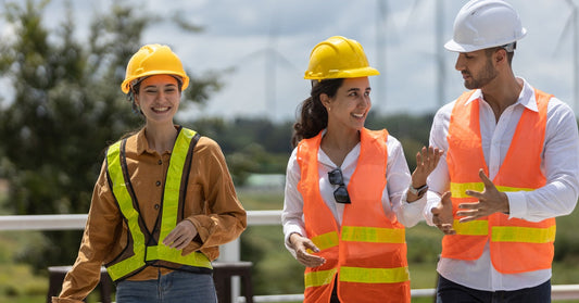 A group of three engineers wearing hard hats and different colored safety vests, talking and walking outdoors.