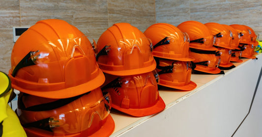 A stack of orange safety hard hats sitting on a shelf. They are double stacked and have safety glasses on the visor.