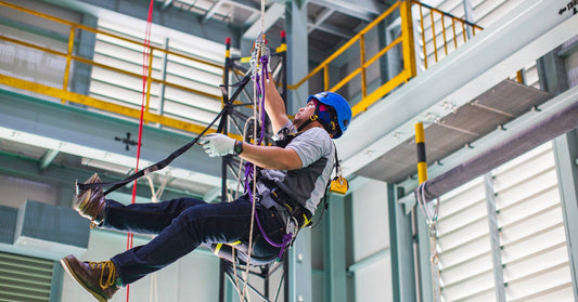 A warehouse employee suspended from the fall protection equipment, including a harness, lanyard, and a safety helmet.