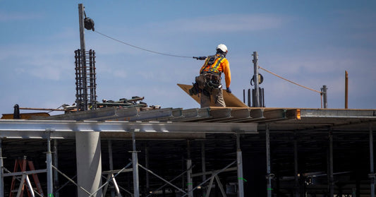 An industrial site engineer on the top of a structure wearing a high-vis safety vest, hard hat, and connected to a lifeline.An industrial site engineer on the top of a structure wearing a high-vis safety vest, hard hat, and connected to a lifeline.