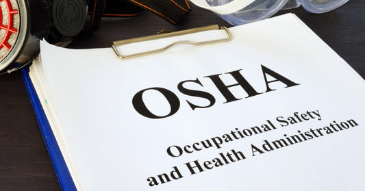 An OSHA certification handbook clipped to a clipboard sits on a desk next to PPE, such as goggles and head gear.