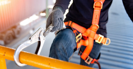 A close-up of a worker wearing a neon orange harness as they try to attach their harness clip to the structure.