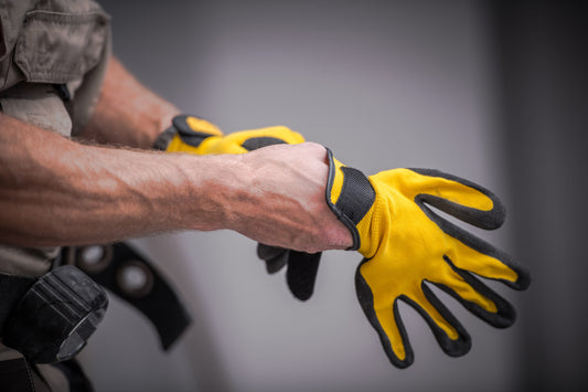 An employee placing yellow and black work gloves on their hands as they get ready to complete a task.