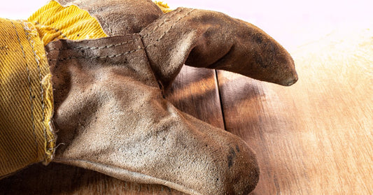 A close-up of a dirty leather work glove. The glove has a cowhide finger and palm construction with a fabric back.